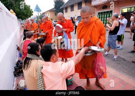 Prozession der buddhistischen Mönche tragen orangefarbene Gewänder in der Morgendämmerung Geschenke auf den Straßen von Luang Prabang, Laos, Asien zu sammeln Stockfoto