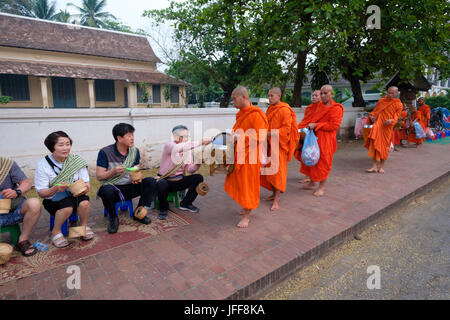 Prozession der buddhistischen Mönche tragen orangefarbene Gewänder in der Morgendämmerung Geschenke auf den Straßen von Luang Prabang, Laos, Asien zu sammeln Stockfoto