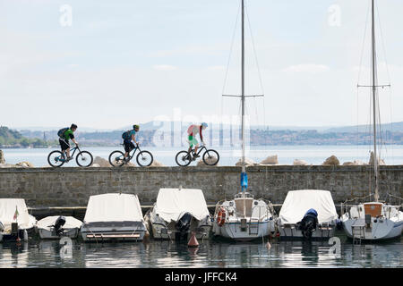 Biker, Fahrrad fahren auf Steg über See mit Segelbooten auf es verankert Stockfoto