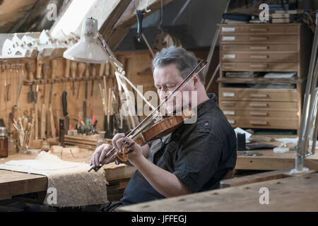 Arbeiter testet und spielt Violine in der Werkstatt Stockfoto