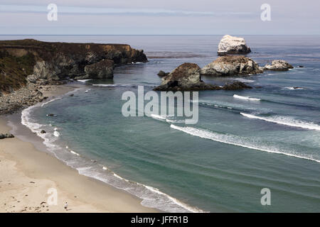 Wellen kommen an Land an der Big Sur Küste. Eine einsame Person Spaziergänge am Sandstrand. Stockfoto