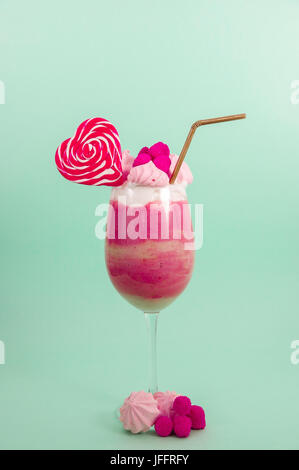 Köstliche hausgemachte extreme Milchshake Erdbeere mit Milchschaum mit einem Kunststoff Stroh und ein Bonbon rosa Blackberry mit einem Herz-Bonbon obendrauf, in ein sof Stockfoto