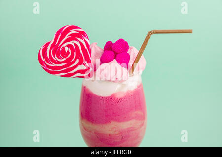 Eine köstliche hausgemachte extreme Milchshake Erdbeere mit Milchschaum mit einem Kunststoff Stroh und ein Bonbon rosa Blackberry mit einem Herz-Bonbon auf Nahaufnahme Stockfoto