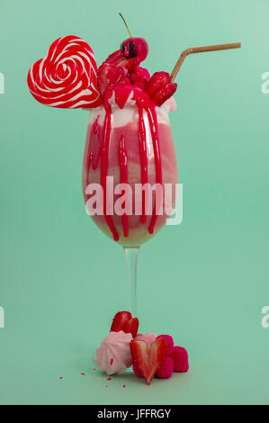 Köstliche hausgemachte extreme Milchshake Erdbeere mit Milchschaum mit einem Kunststoff Stroh und ein Bonbon rosa Blackberry mit einem Herz-Bonbon obendrauf, in ein sof Stockfoto