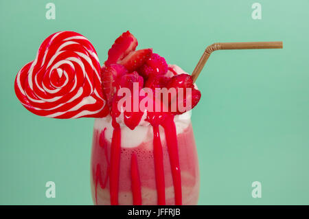 Köstliche hausgemachte extreme Milchshake Erdbeere mit Milchschaum mit einem Kunststoff Stroh und ein Bonbon rosa Blackberry mit einem Herz-Bonbon obendrauf, in ein sof Stockfoto