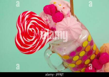 Nahaufnahme von einen köstlichen hausgemachten extreme Milchshake Erdbeere in einem Glas mit einem Blackberry Bonbons über Milchschaum mit einem Kunststoff Stroh und ein rosa bl Stockfoto