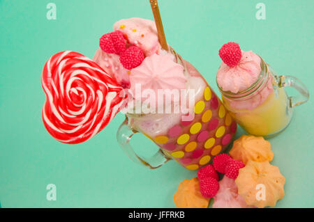 Nahaufnahme von einen köstlichen hausgemachten extreme Milchshake Erdbeere in einem Glas mit einem Blackberry Bonbons über Milchschaum mit einem Kunststoff Stroh und ein rosa bl Stockfoto