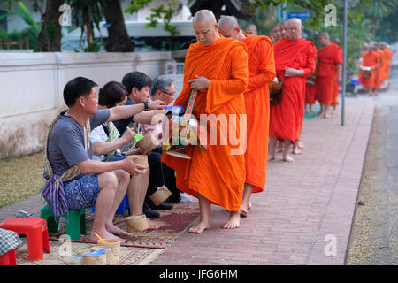 Prozession der buddhistischen Mönche tragen orangefarbene Gewänder in der Morgendämmerung Geschenke auf den Straßen von Luang Prabang, Laos, Asien zu sammeln Stockfoto