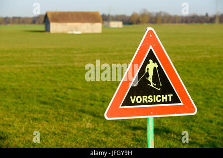 Straßenschild in Straße warnt vor Kreuzfahrt Skifahrer auf der Loipe, grüne Wiesen, frühlingshafte Temperaturen um 15 Grad, nur wenige Tage vor Weihnachten 2015 Stockfoto