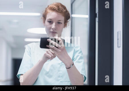Junge Krankenschwester mit Mobiltelefon im Krankenhaus Stockfoto