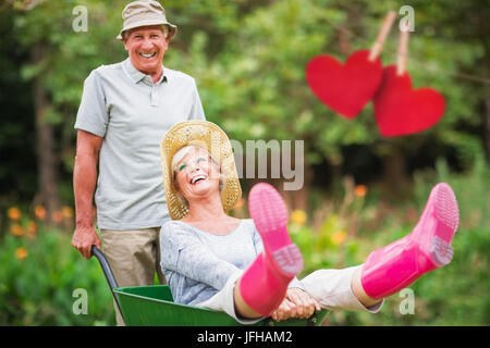 Zusammengesetztes Bild von glücklichen senior paar spielen mit einer Schubkarre Stockfoto