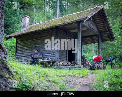 Mountain Biker Lesung Magazin beim Sitzen vor einer Hütte im Wald Stockfoto