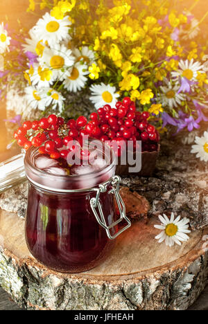 Der Saft aus den Beeren des Viburnum in Glasbehältern auf einer Serviette neben einem Bouquet von wilden Blumen auf einem Holzständer. Rustikale. Die vertikalen Rahmen Stockfoto