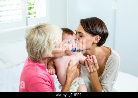 Großmutter und Mutter küssen Baby Boy auf Bett Stockfoto