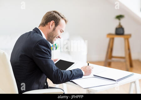 Geschäftsmann schreiben in einem Tagebuch und mit Hilfe eines digitalen Tablet Stockfoto