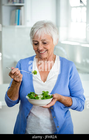 Ältere Frau essen Salat stehend in Küche Stockfoto