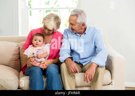 Glückliche Großeltern betrachten Baby bei der Standortwahl auf sofa Stockfoto