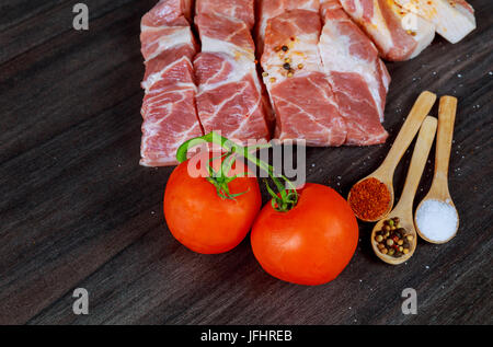 Rohes Schweinefleisch Speckscheiben, Speck, Gewürze, Pfefferkörner, Knoblauch, Lorbeerblätter und rote frische Kirschtomaten auf Schiefer Tafel, Nahaufnahme, hohe Angl Stockfoto