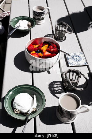 weißen hölzernen Tischplatte mit einem gesunden Frühstück auf sie in der Mitte eine bunte Obstschale mit Erdbeeren, Heidelbeeren und Pfirsiche in Stockfoto