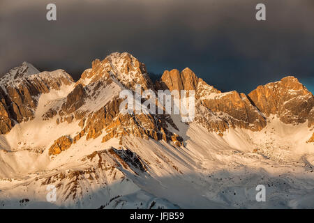 Eine feurige fallenden Winter Sonnenuntergang in Richtung Sasso di Valfredda, vom linken Punta Jigole, Sasso Vernale, Cima Ombrettola, Sasso Valfredda und Formenton, hinter ihnen, Wolken die immense Südwand der Marmolada, Dolomiten, Italien Stockfoto