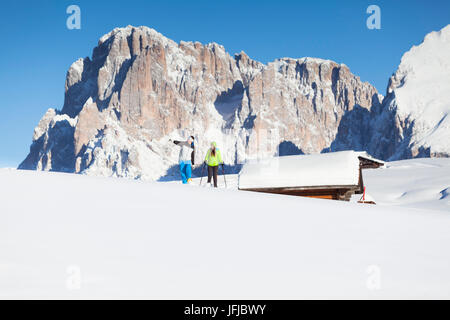 zwei Modelle sind in den frischen Schnee auf der Seiser Alm mit einigen Hütten und den Langkofel Peak im Hintergrund Bozen Provinz, Südtirol, Trentino Alto Adige, Italien, Europa Fuß Stockfoto