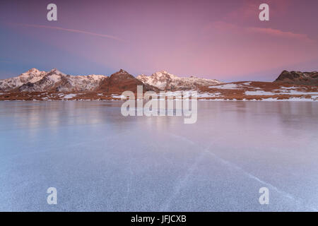 Die schneebedeckten Gipfel spiegeln sich auf der Eisfläche des Andossi-Sees in der Morgendämmerung Spluga Tal Valtellina Lombardei Italien Europa Stockfoto