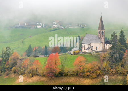 Kirche, umgeben von herbstlichen Bäumen und Nebel, St. Magdalena, Funes, Bozen, Trentino Alto Adige - Südtirol, Italien, Europa, Stockfoto