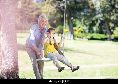 Großvater Drängen seiner Enkelin auf Schaukel Stockfoto