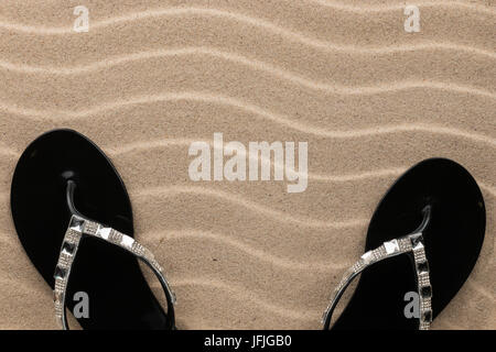 Paar schwarze Strand Flip-Flops, besetzt mit Strasssteinen auf dem Sand, mit Platz für Ihren Text stehen Stockfoto