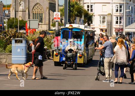 Weymouth, Dorset, UK. 1st July 2017.    UK Weather - A man in a mobility scooter driving in front of the land train on the Esplanade on a day of blue skies and hot sunshine at the seaside resort of Weymouth in Dorset.  Photo Credit: Graham Hunt/Alamy Live News Stockfoto