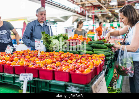 Montreal, Kanada - 28. Mai 2017: Mann, Verkauf von Produkten durch Obststand mit Frau kaufen Gurken auf Jean-Talon Bauernmarkt mit displays Stockfoto