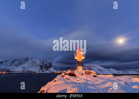 Leuchtturm und Vollmond in der Polarnacht mit dem Dorf Reine im Hintergrund Nordland Lofoten Inseln Norwegen Europa Stockfoto
