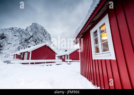 Wolken auf den typischen roten Häusern der Fischer namens Fischerorten umgeben von schneebedeckten Hamnøy Lofoten Inseln Norwegen Nordeuropa Stockfoto