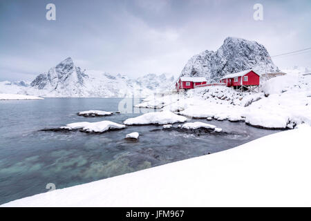 Die schneebedeckten Gipfel und gefrorene Meer umrahmen die typischen Fischer-Häuser genannt Rorbu Hamnøy Lofoten Inseln Norwegen Nordeuropa Stockfoto