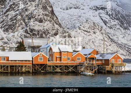 Typische Holzhäuser der Fischer namens Rorbu umrahmt von schneebedeckten Gipfeln und den kalten See Hamnoy Reine Lofoten Inseln Norwegen Europa Stockfoto