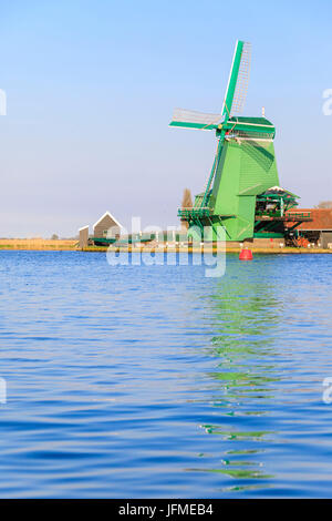 Typische Windmühle spiegelt sich im blauen Wasser des Flusses Zaan im Frühjahr Zaanse Schans Nord Holland-die Niederlande Europa Stockfoto