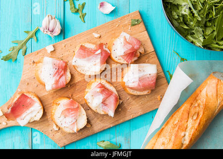 Foto von Sandwiches mit Speck auf blauen Holztisch mit Rucola-Salat Stockfoto