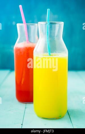 Flasche frisch gepressten Orangensaft und Roter Beete, frisch gepressten Saft im Glas auf blauem Hintergrund. Gesundes rohes Gemüse und Obst trinken für Entgiftung auf eine Stockfoto