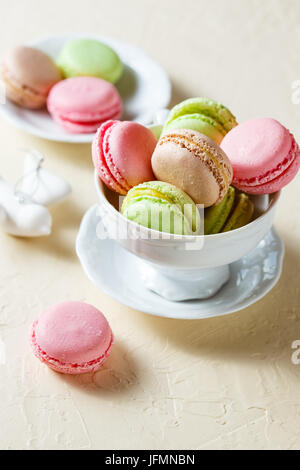 Bunte Cookies Macaron in das weiße Porzellan Tasse auf einem hellen Hintergrund Stockfoto
