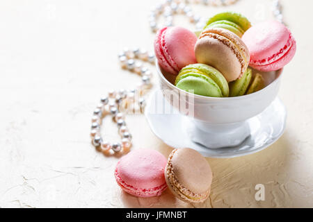 Bunte Cookies Macaron in das weiße Porzellan Tasse und Perlen auf einem hellen Hintergrund Stockfoto