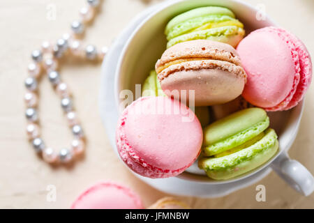 Bunte Cookies Macaron in das weiße Porzellan Tasse und Perlen auf einem hellen Hintergrund Stockfoto