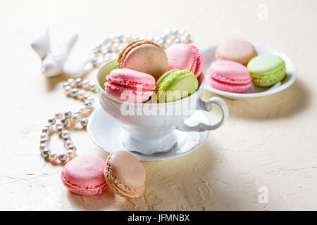 Bunte Cookies Macaron in das weiße Porzellan Tasse und Perlen auf einem hellen Hintergrund Stockfoto