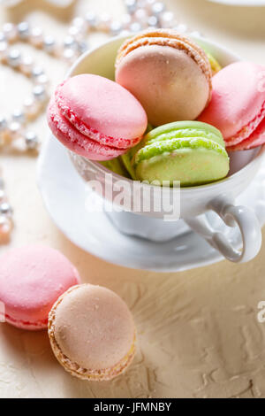Bunte Cookies Macaron in das weiße Porzellan Tasse und Perlen auf einem hellen Hintergrund Stockfoto