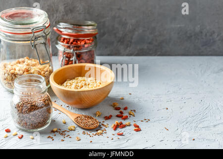 Goji-Beeren, Müsli, Leinsamen, Pinienkerne in Gläsern auf grauem Hintergrund Stockfoto