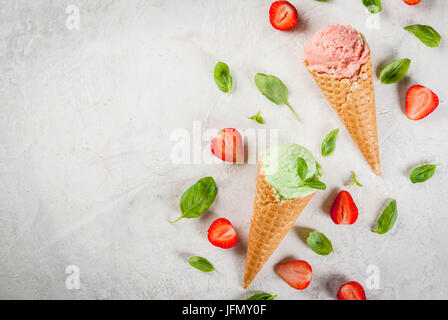 Sommer frische Desserts. Grüne Basilikum und roten Erdbeereis in einem Kegel. Auf einem weißen Stein Tisch mit Basilikum und frischen Erdbeeren um. Auf Stockfoto