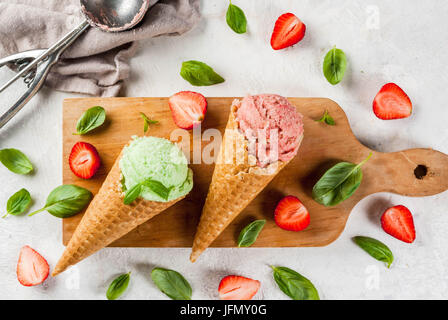 Sommer frische Desserts. Grüne Basilikum und roten Erdbeereis in einem Kegel. Auf einem weißen Stein Tisch mit Basilikum und frischen Erdbeeren um. Auf Stockfoto