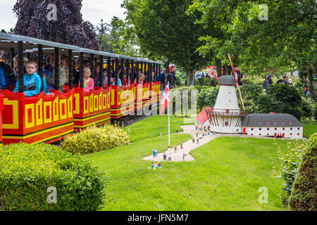 Billund, Dänemark - 27. Juli 2017: Spielzeugeisenbahn mit Passanten durch Legoland Freizeitpark. Wassermühle gebaut aus Lego-Steinen in der grünen gro Stockfoto