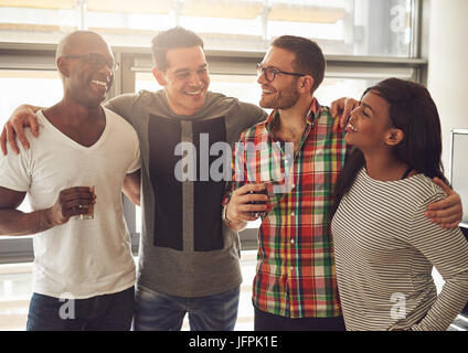 Fröhliche junge Menschen stehen im Büro mit den Getränken. Stockfoto