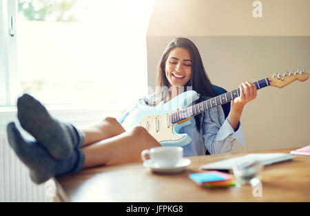Schöne Mädchen singen während des Spielens ihre e-Gitarre mit Füßen auf Tisch Stockfoto