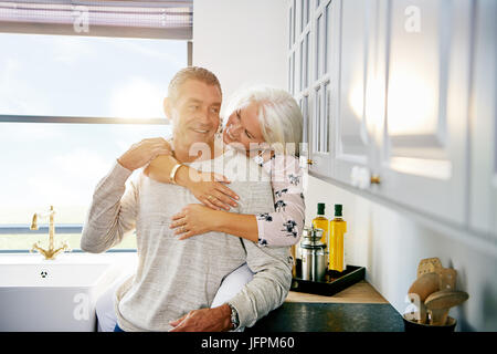 Inhalt älteres paar lächelnd und gemeinsam einen liebevollen Moment zusammen und entspannen Sie in ihrer Küche zu Hause Stockfoto